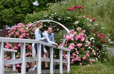 Ein Paar genießt einen Spaziergang durch das Rosenmeer im Rosarium Uetersen und macht Pause auf einer weißen Brücke.