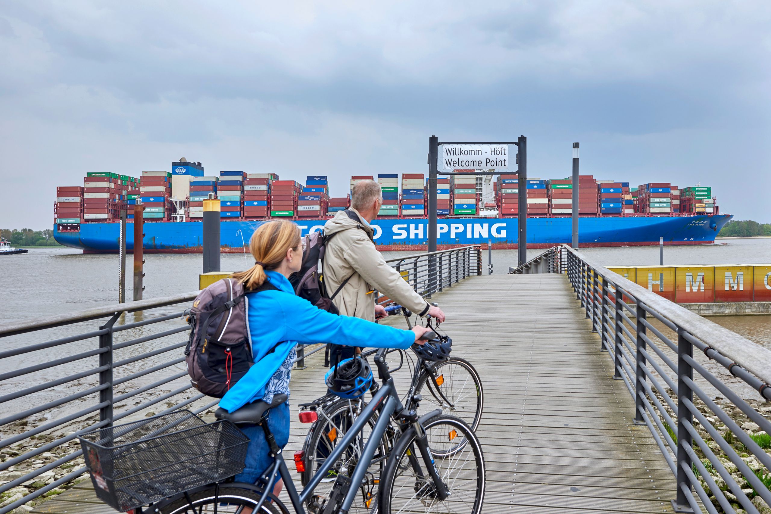 Radfahrer beobachten am Willkomm-Höft ein Schiff auf der Elbe.