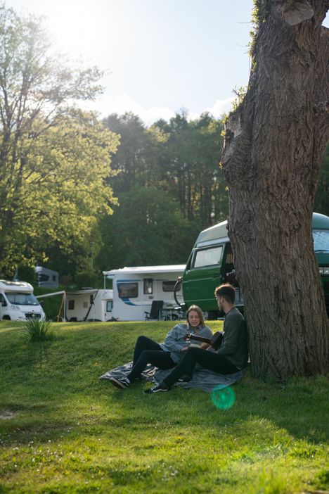 Paar genießt die Zeit auf dem Campingplatz und ist sitzend an einen Baum gelehnt. 