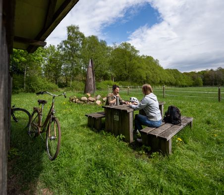 Zwei Radfahrer trinken auf einem malerischen Rastplatz am Ochsenweg bei Neumünster einen Kaffee, im Hintergrund ist eine Ochsen-Hörner-Skulptur zu sehen.